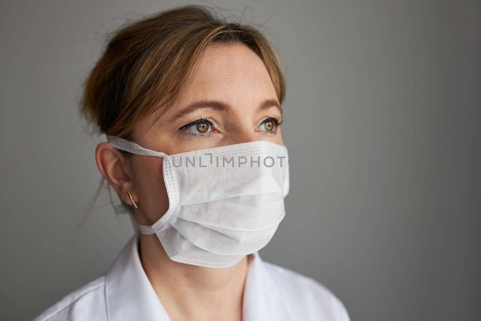 Doctor with face covered with mask. Portrait of young woman wearing the uniform and mask to avoid virus infection and to prevent the spread of disease. Real people, authentic situations