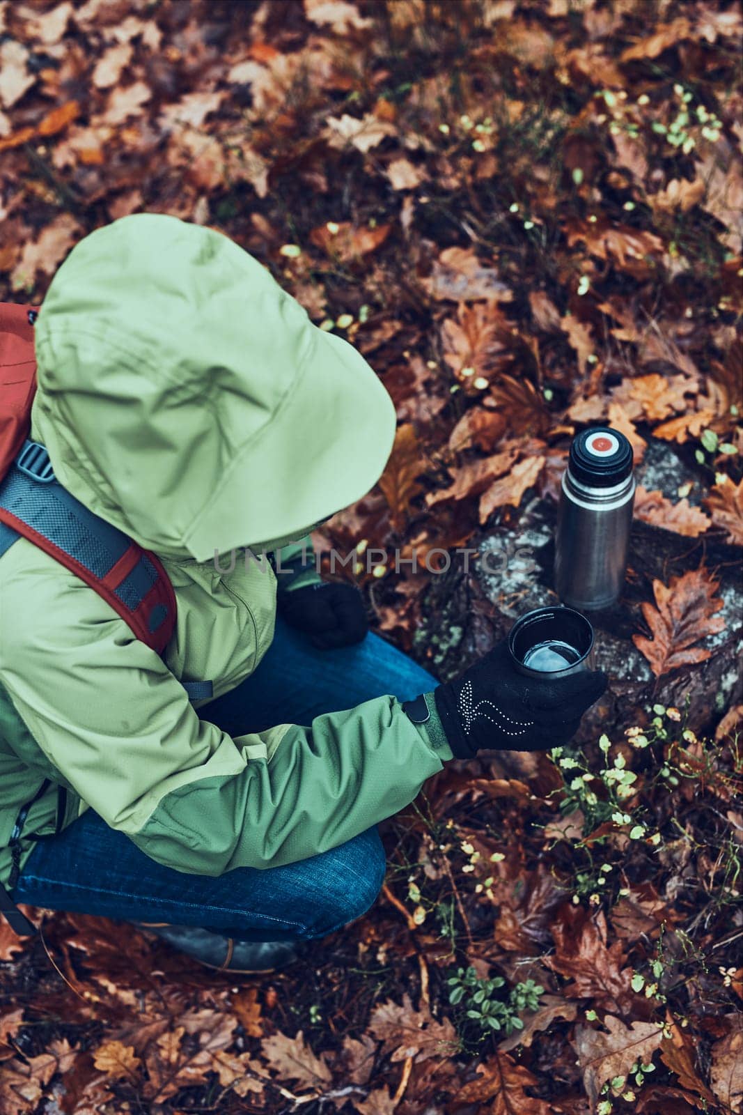 View from above of woman with backpack having break during autumn trip drinking a hot drink from thermos flask on autumn cold day. Active middle age woman wandering around a forest actively spending time