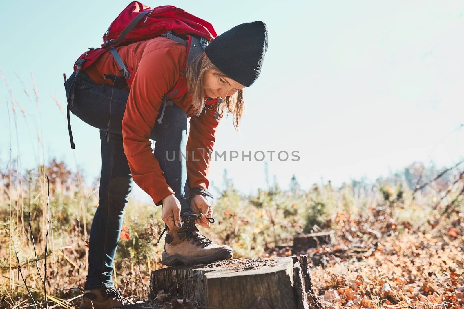 Woman tying laces on hiking boots while hike on vacation trip. Hiker with backpack taking break during walking. Active leisure time close to nature