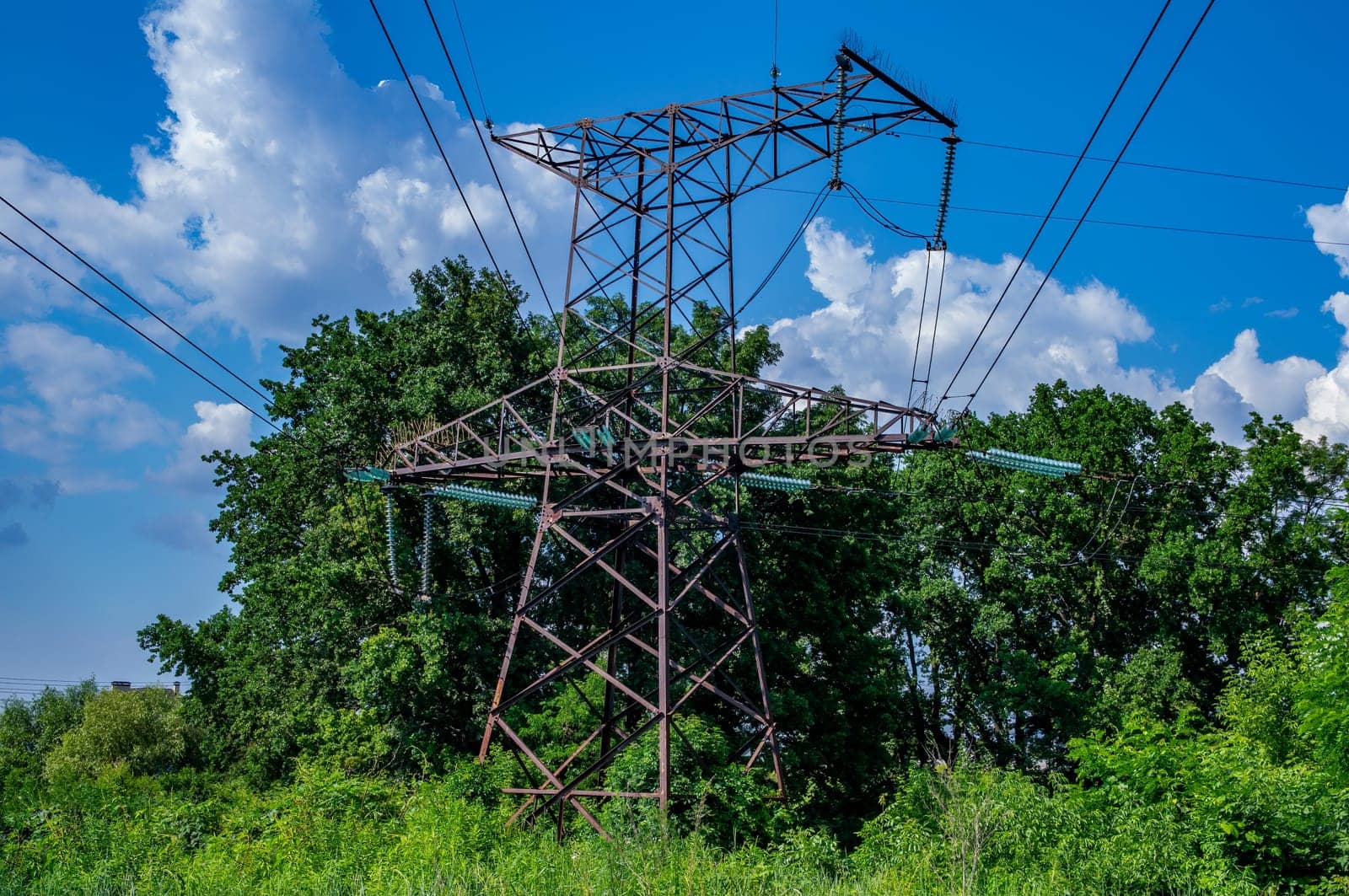 Tower with high-voltage energy transmission wires against the blue sky. High-voltage tower. Electrical wires and fuses. Energy business. Energy industry. Import and export of energy. Blue sky.