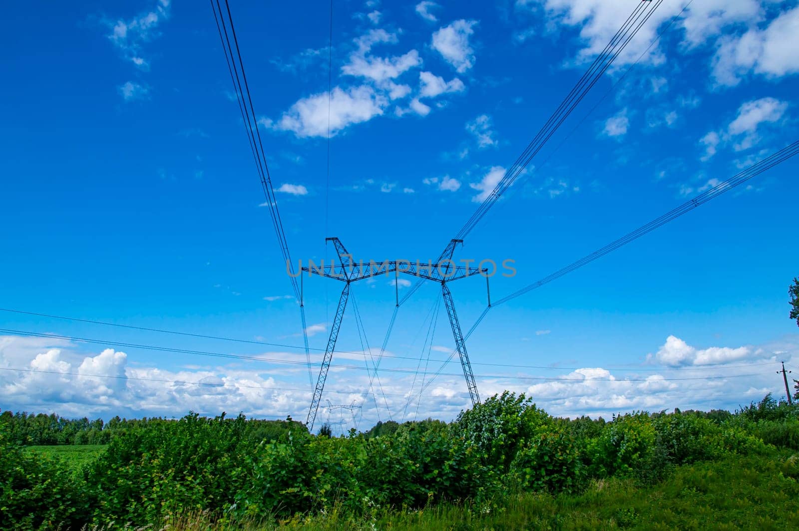 Tower with high-voltage energy transmission wires against the blue sky. High-voltage tower. Electrical wires and fuses. Energy business. Energy industry. Import and export of energy. Blue sky.