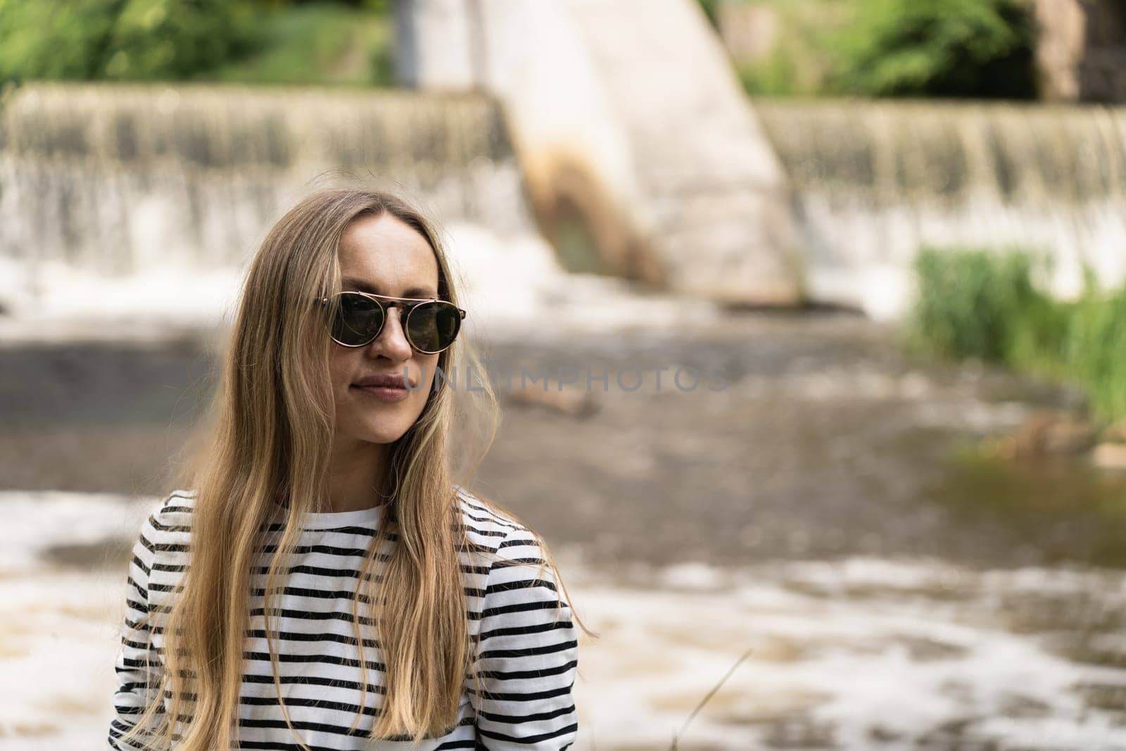 Portrait of a woman in a striped top and sunglasses in front of the dam by the river.