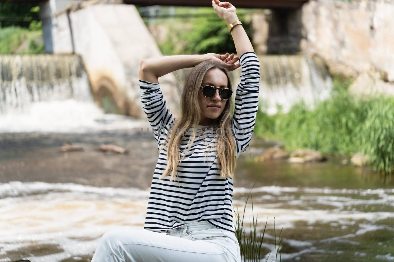 A woman relaxes and rests, sitting near the river in early summer.