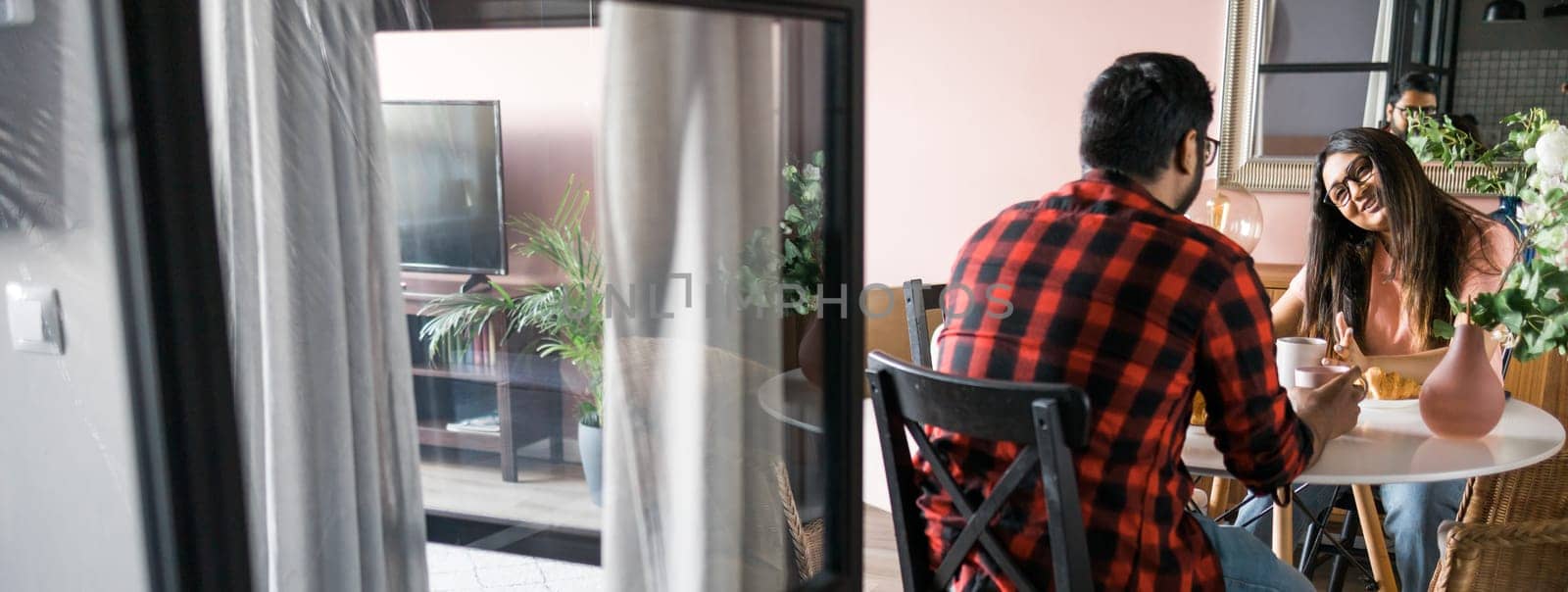 Young diverse loving couple eating croissant and talks together at home in breakfast time. Communication and relationship