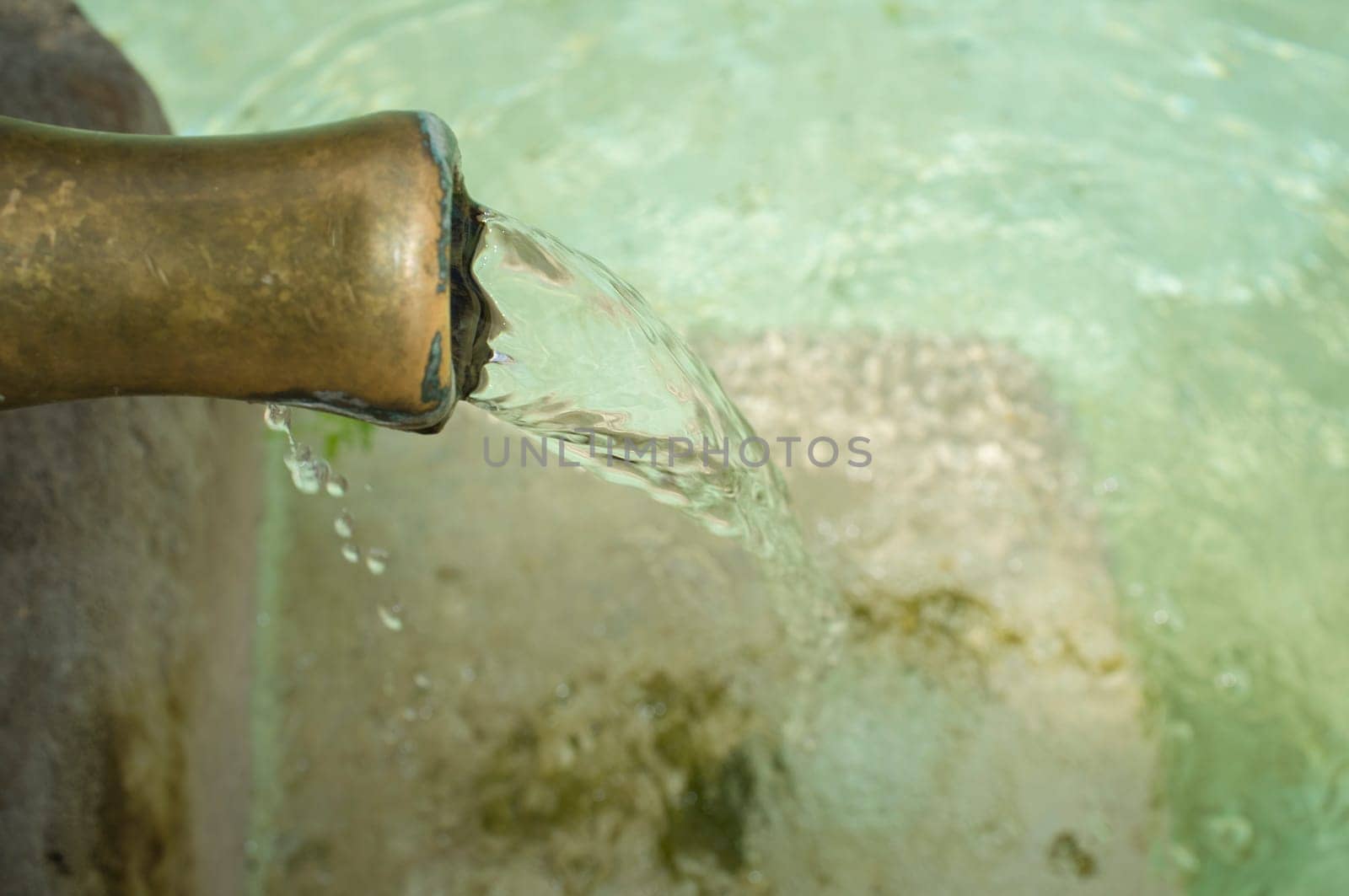 Water permanently flowing from a pipe of a public fountain. Concept of drinking water supply in ancient times