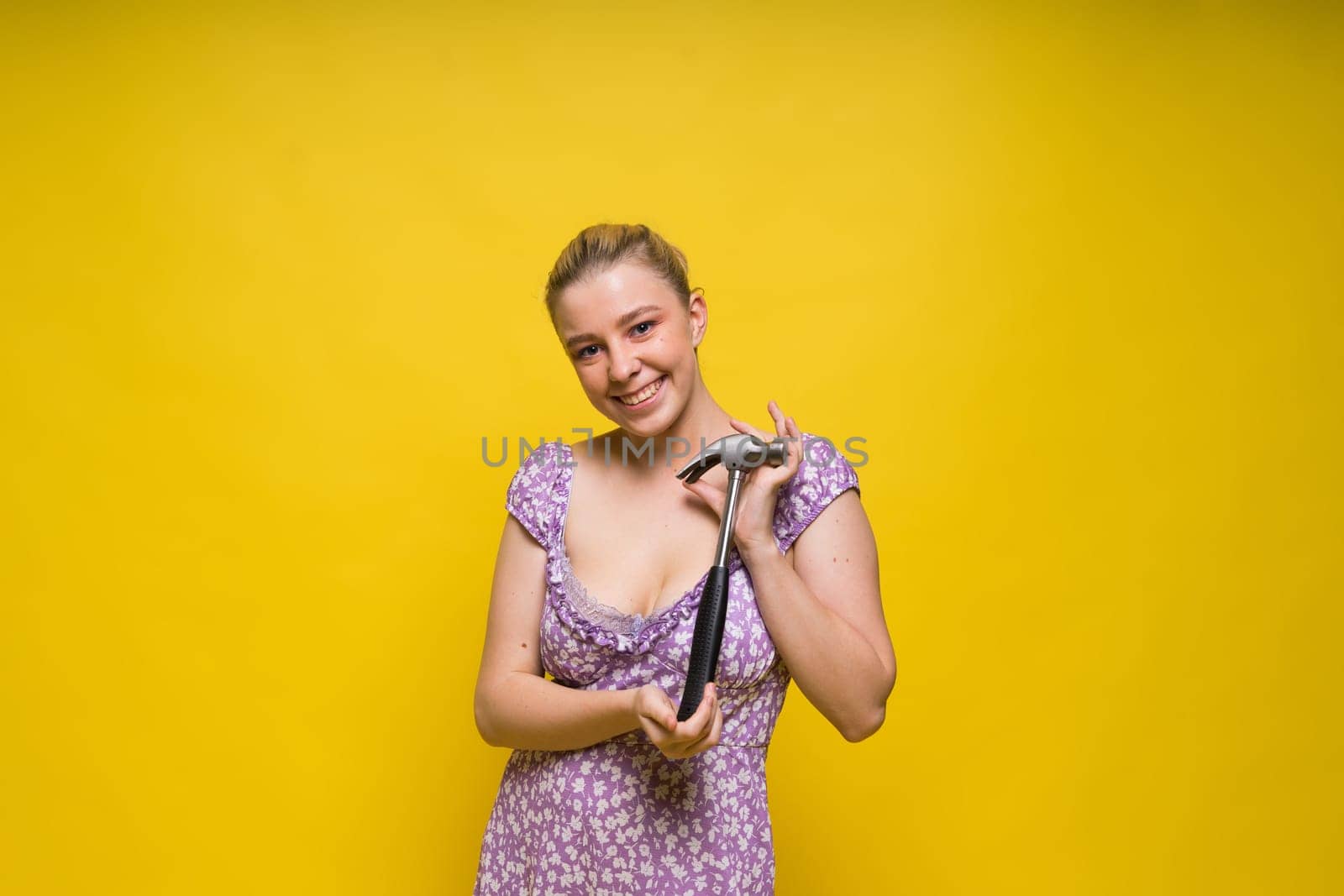 Beautiful seductive female holding hammer, isolated on a yellow and red