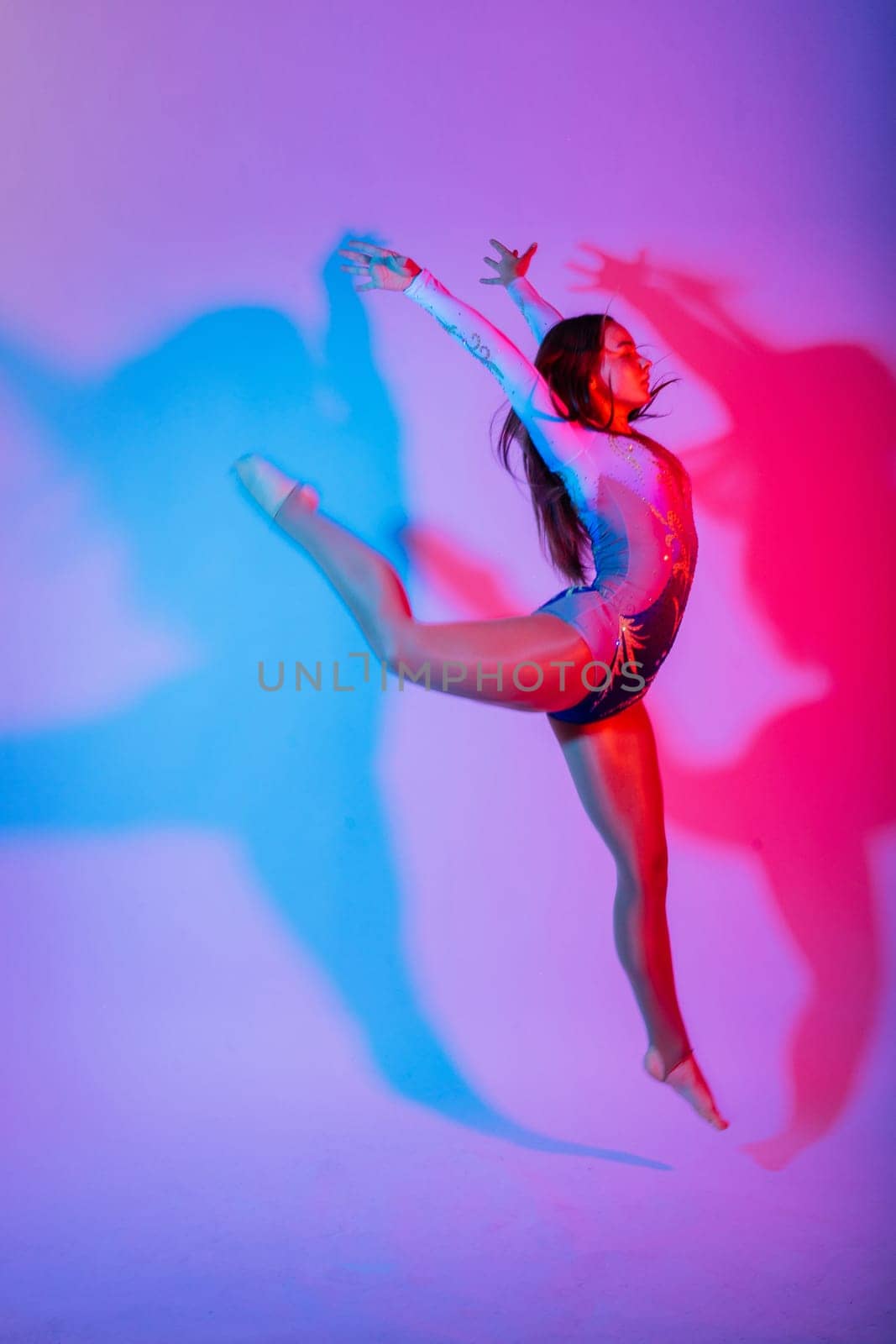 Flexible girl, rhythmic gymnastic artist jumping on white dark background. Grace in motion, action.