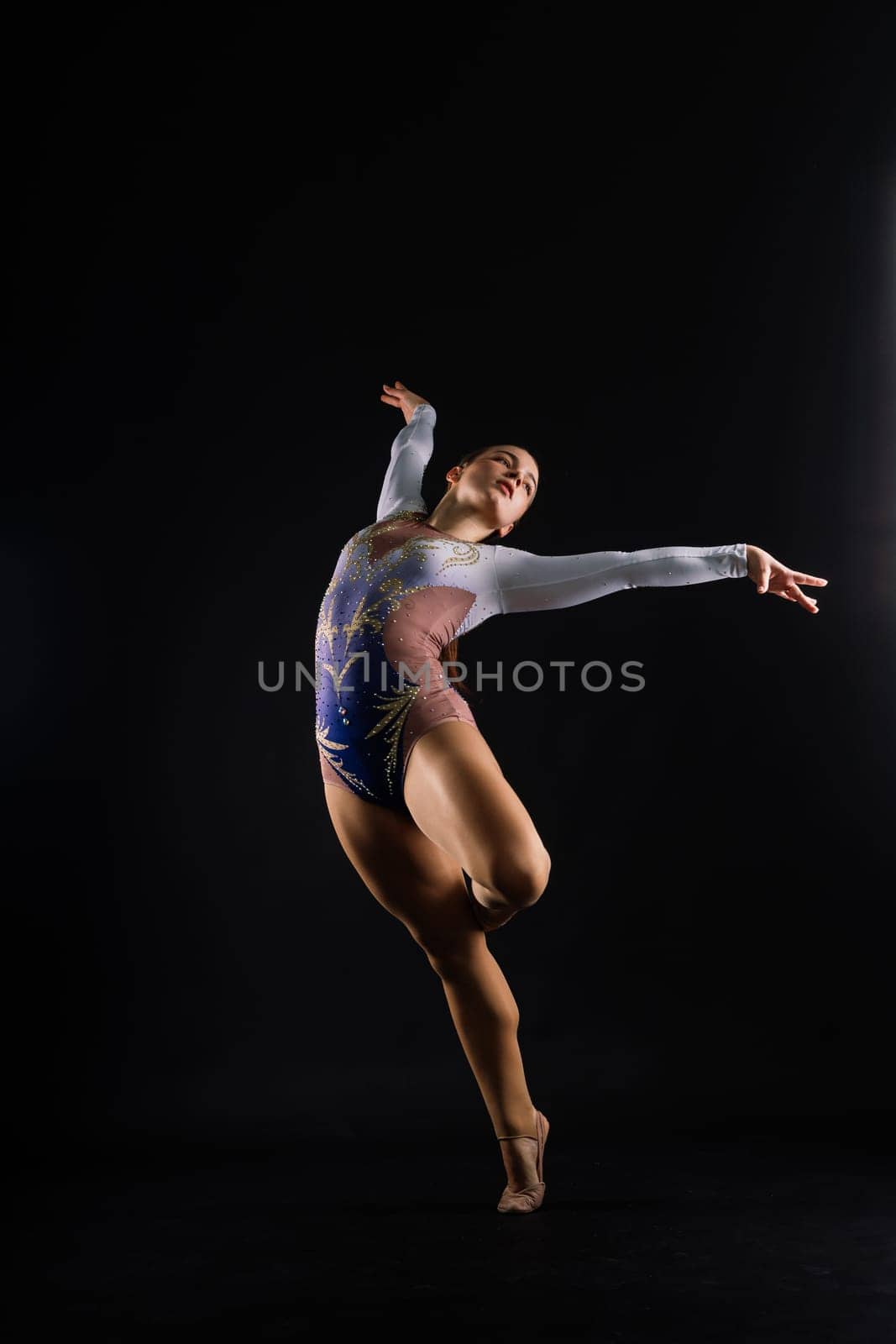 Flexible girl, rhythmic gymnastic artist jumping on white dark background. Grace in motion, action.