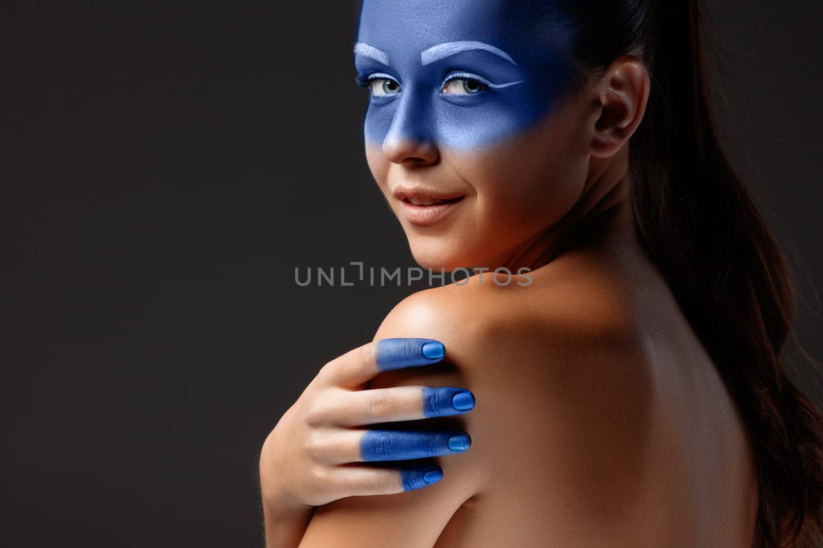 Portrait of a young woman who is posing covered with blue paint in the studio on a black background. girl&#39 s hand  painted blue