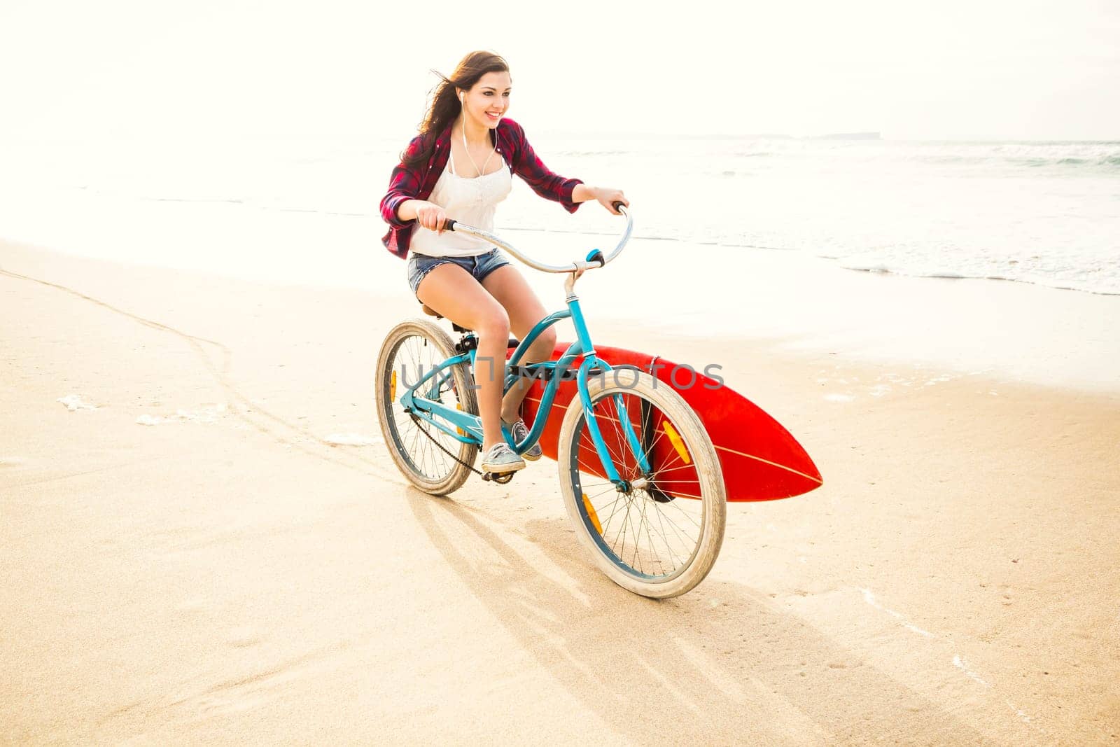 Surfer young woman riding her bicycle on the beach