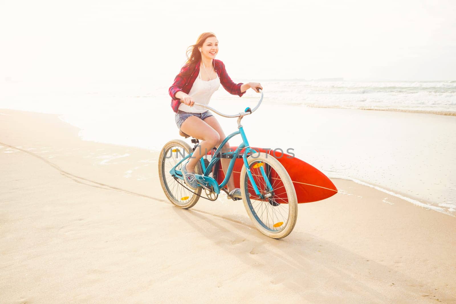 Surfer young woman riding her bicycle on the beach