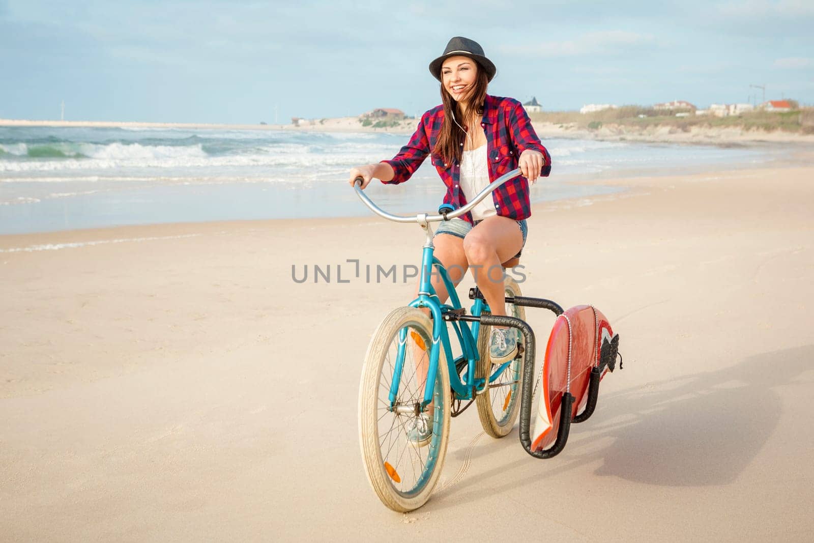 Surfer young woman riding her bicycle on the beach