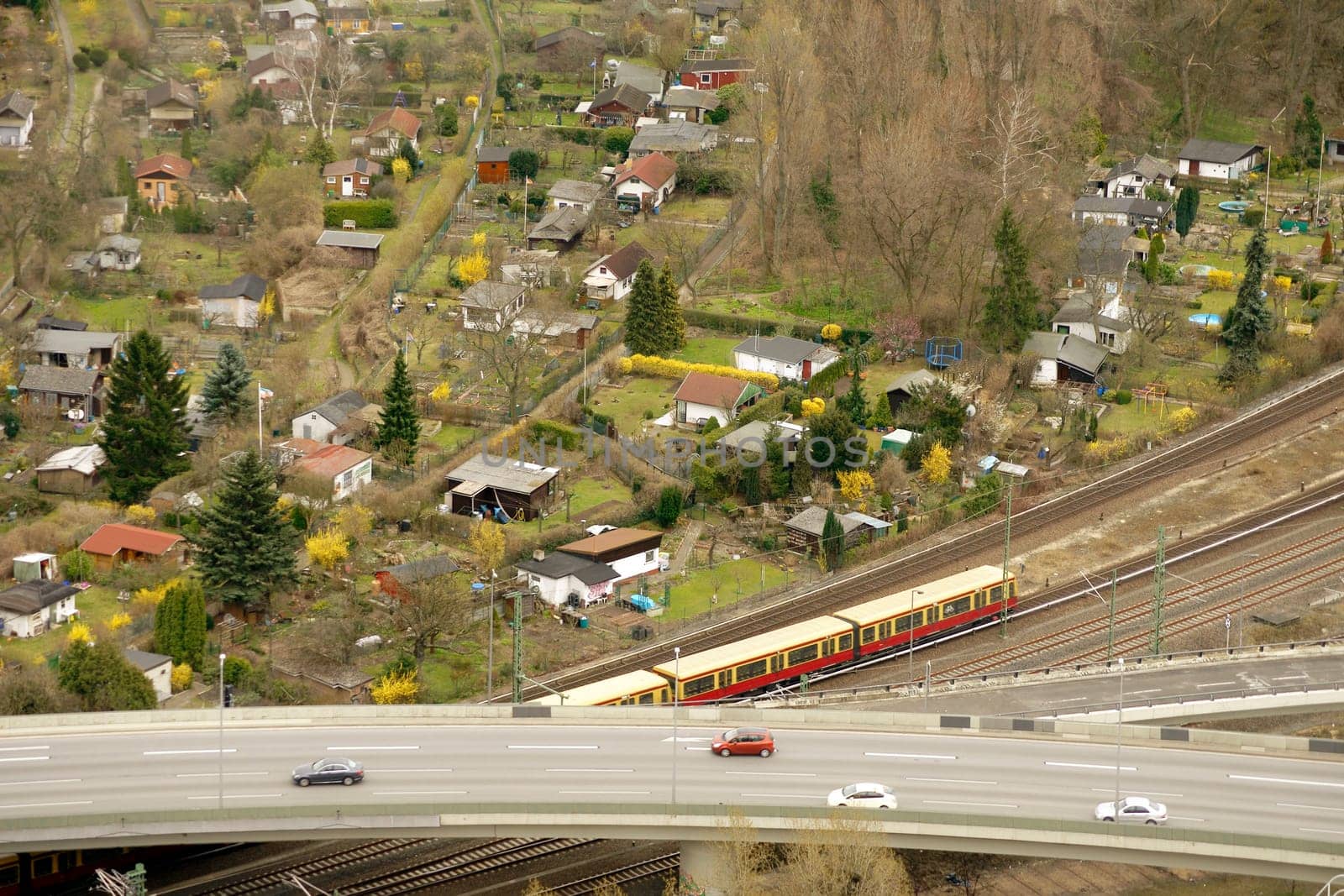 The aerial view of a garden area in Berlin with an adjacent motorway and a rail network with an S-Bahn.