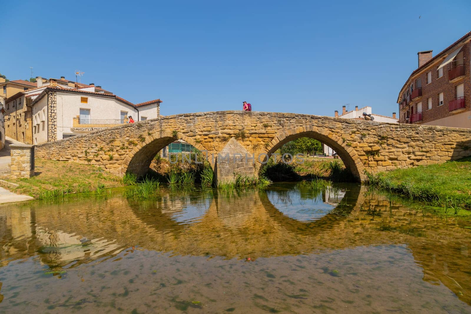 Navarre, Spain, 26 August, 2022: Pilgrims walking over the medieval bridge part of the pilgrim route the Camino de Santiago the way of St James in the village of Villatuerta. Spain