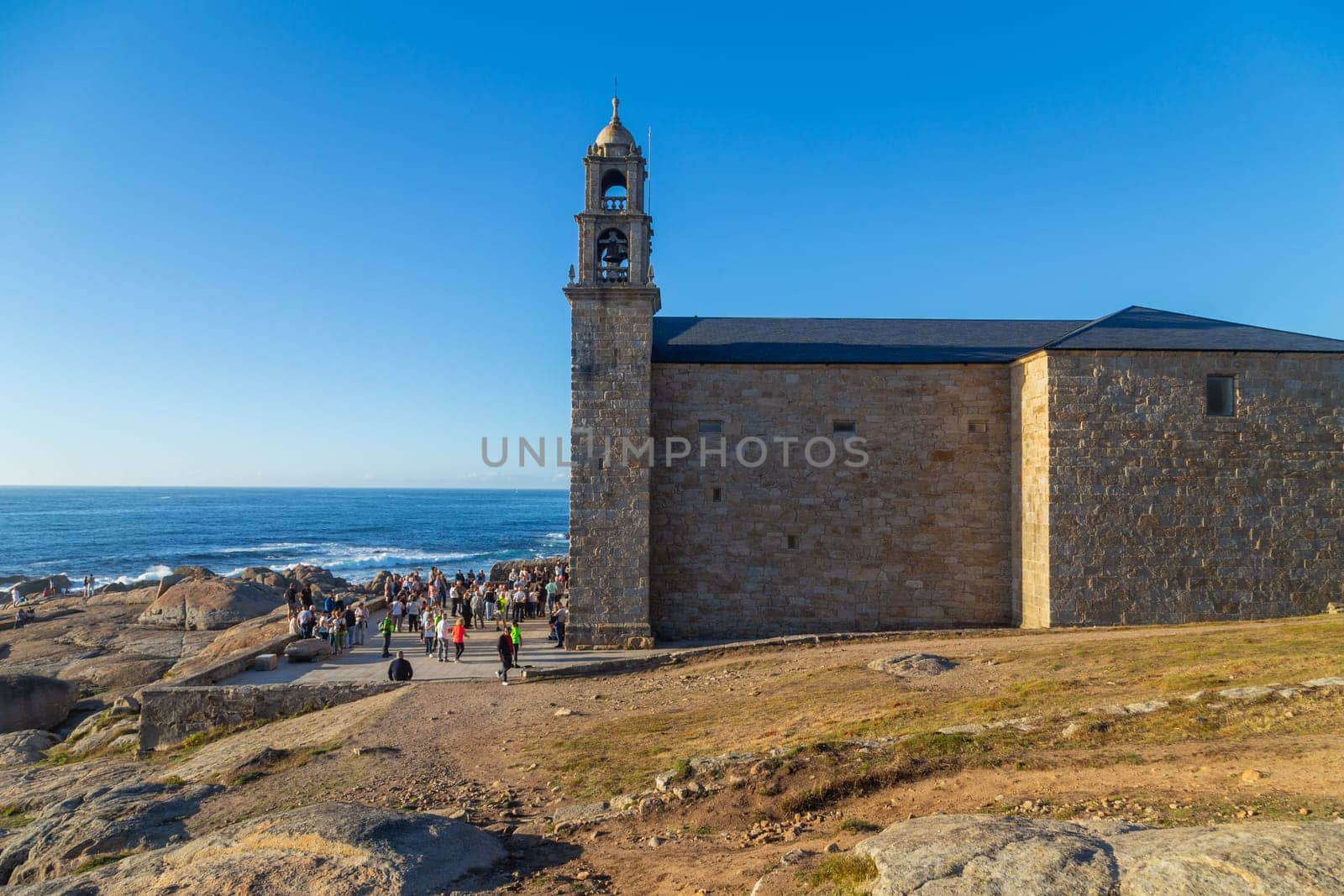 Muxia, A Coruna - Spain August 30, 2022: Virxe de la Barca Sanctuary on Atlantic coast rocks in the foreground afternoon light