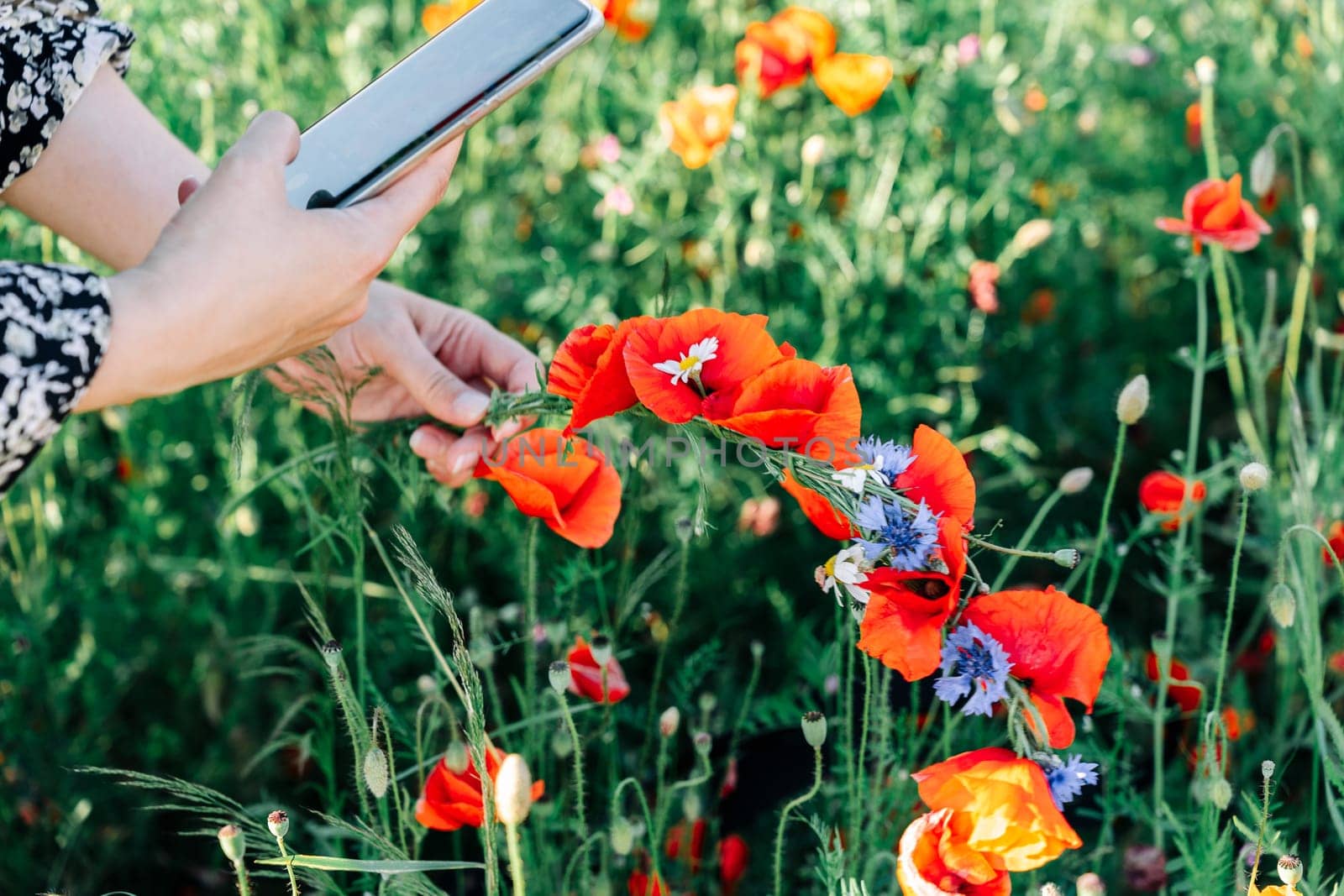 A woman takes a photo on her mobile phone of a wreath of wildflowers, red poppies and blue cornflowers