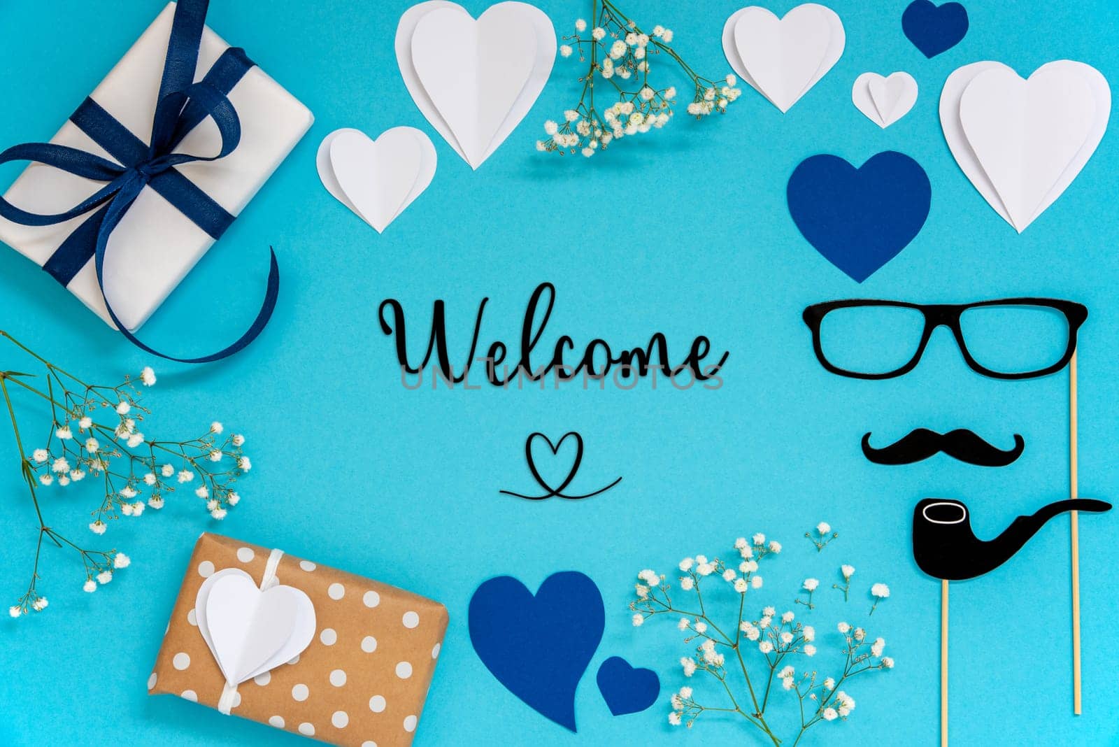 Flat Lay With English Text Welcome. Blue Accessories Like Presents, Hearts, Flowers And Male Decoration Like Mustache. Flat Lay With Turquoise Paper Background.