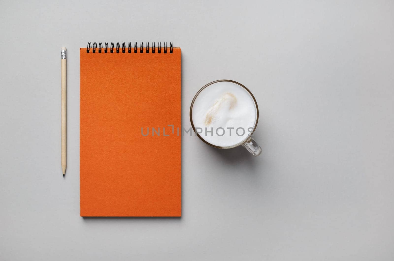 Photo of blank orange sketchbook, coffee cup and pencil on gray paper background. Flat lay.