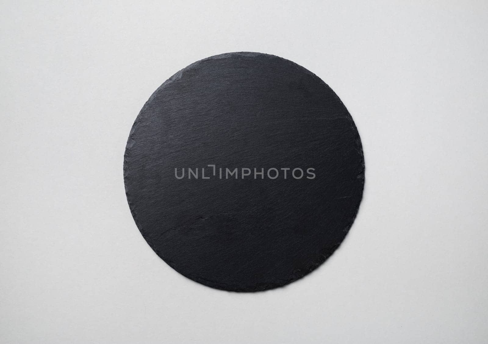 Photo of round slate plate on gray paper background. Copy space. Flat lay.