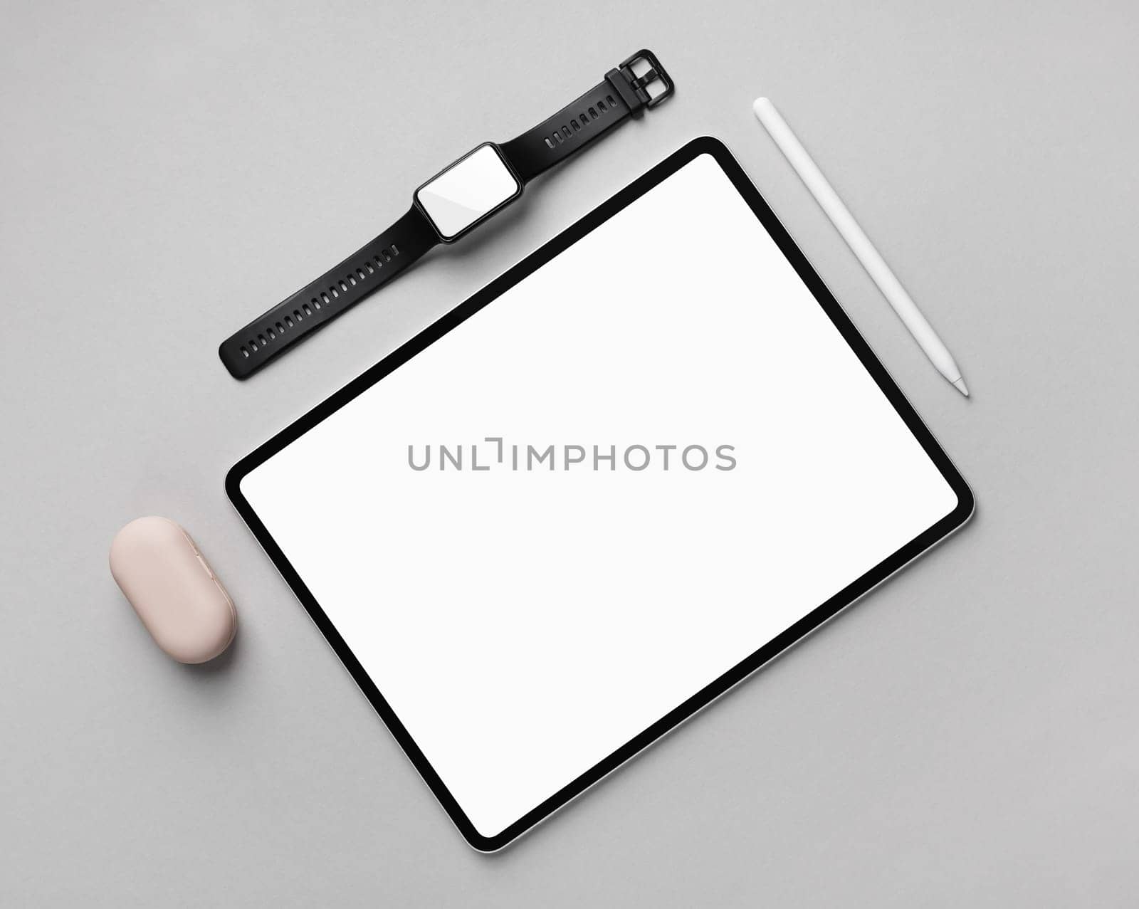 Tablet computer with blank white screen, fitness bracelet and stylus pen on gray paper background. Top view. Flat lay.