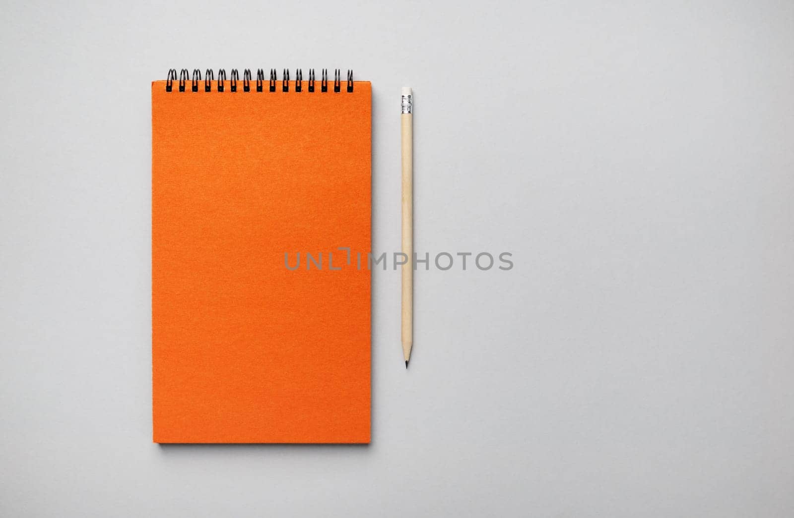 Blank orange notebook and pencil on gray paper background. Template for branding design. Flat lay.