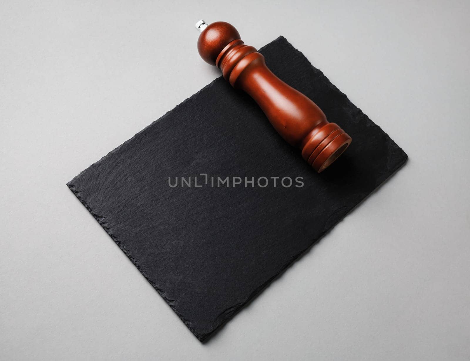 Pepper mill and black stone slate plate on gray paper background.