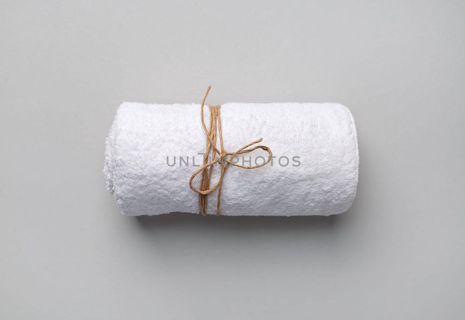 Rolled white towel tied with a rope on gray paper background.