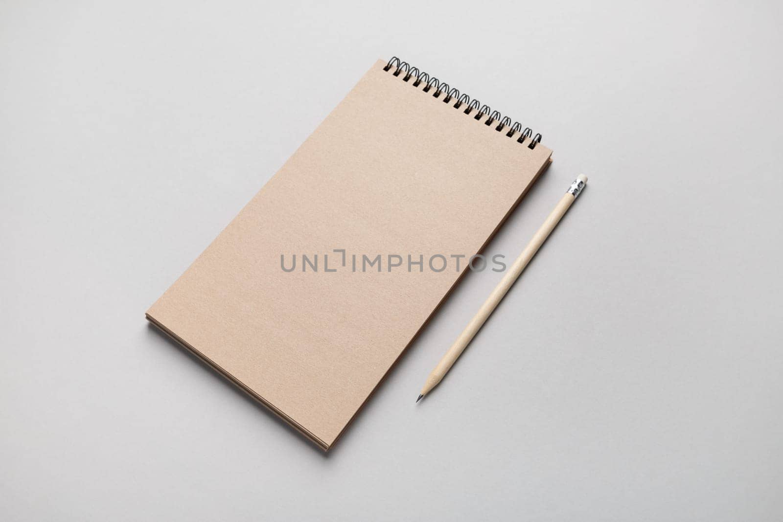 Blank kraft notebook and pencil on gray paper background. Mock-up for design presentations and portfolios.