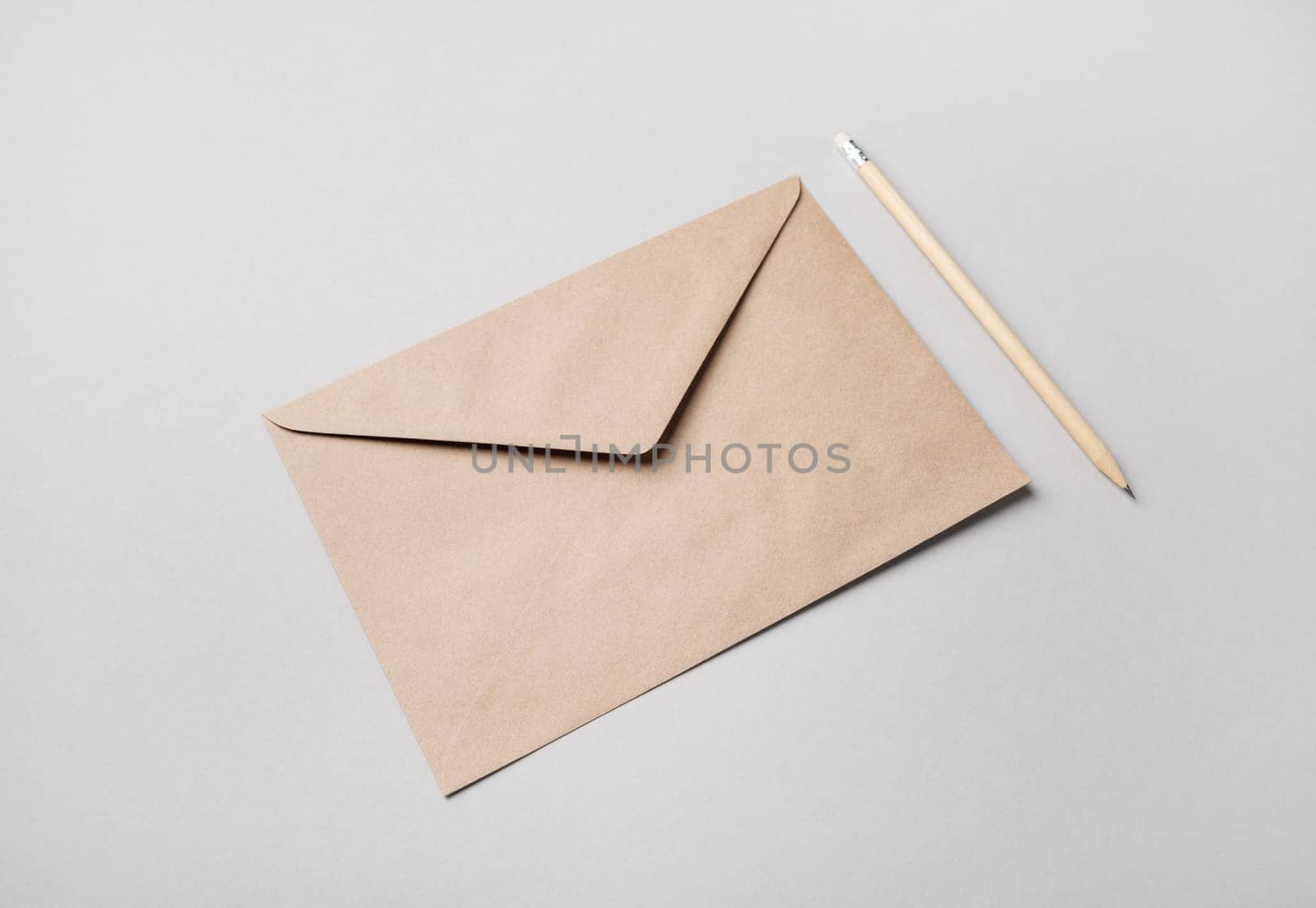 Blank kraft paper envelope and pencil on gray paper background. Mockup for your design.