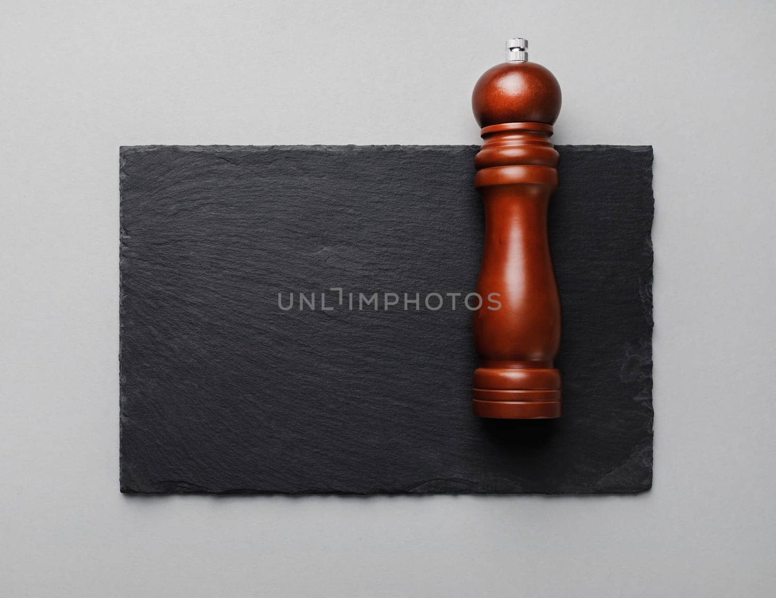 Photo of pepper mill and slate plate on gray paper background. Copy space. Flat lay.