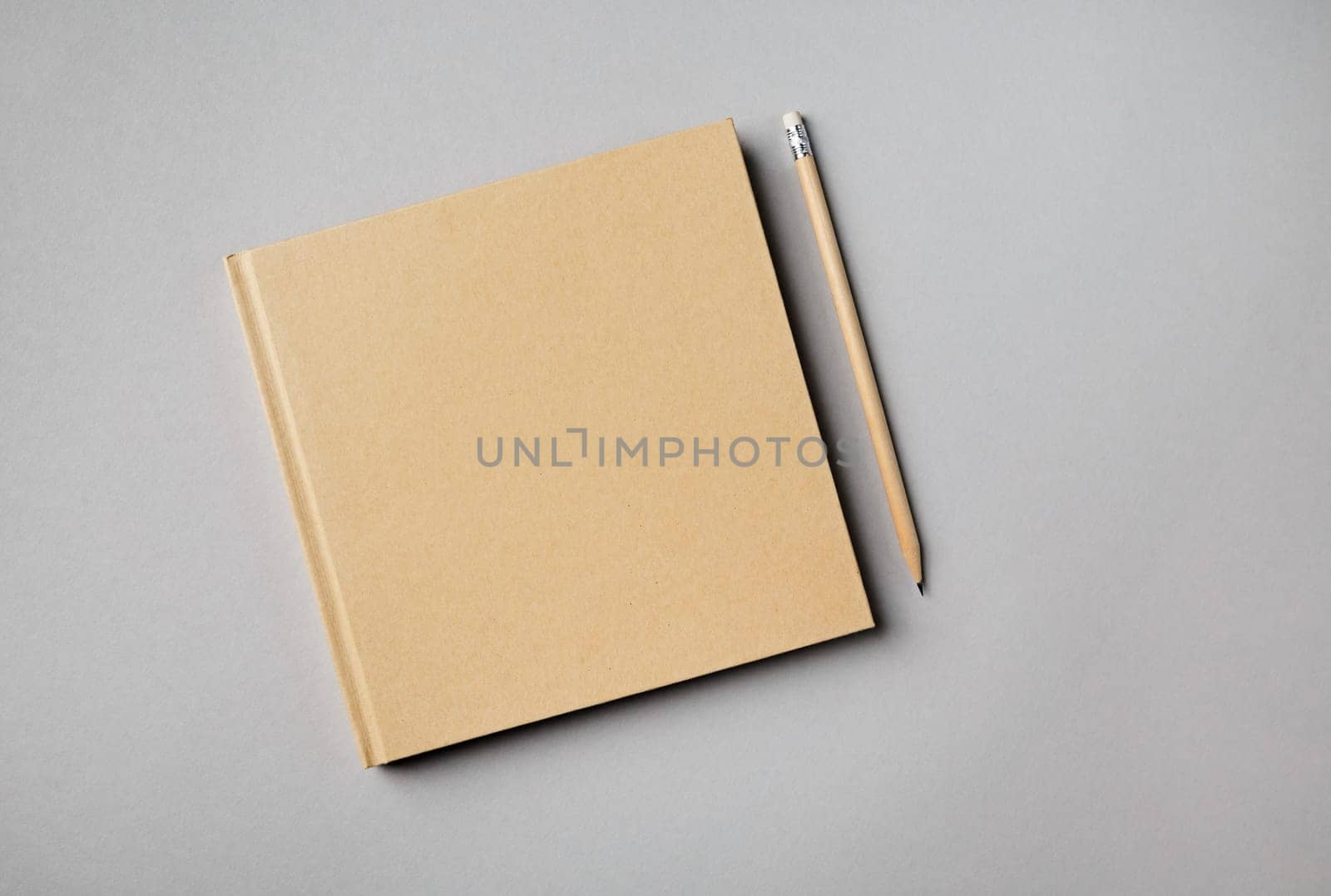 Mockup of closed blank square notebook and pencil on gray paper background. Flat lay.