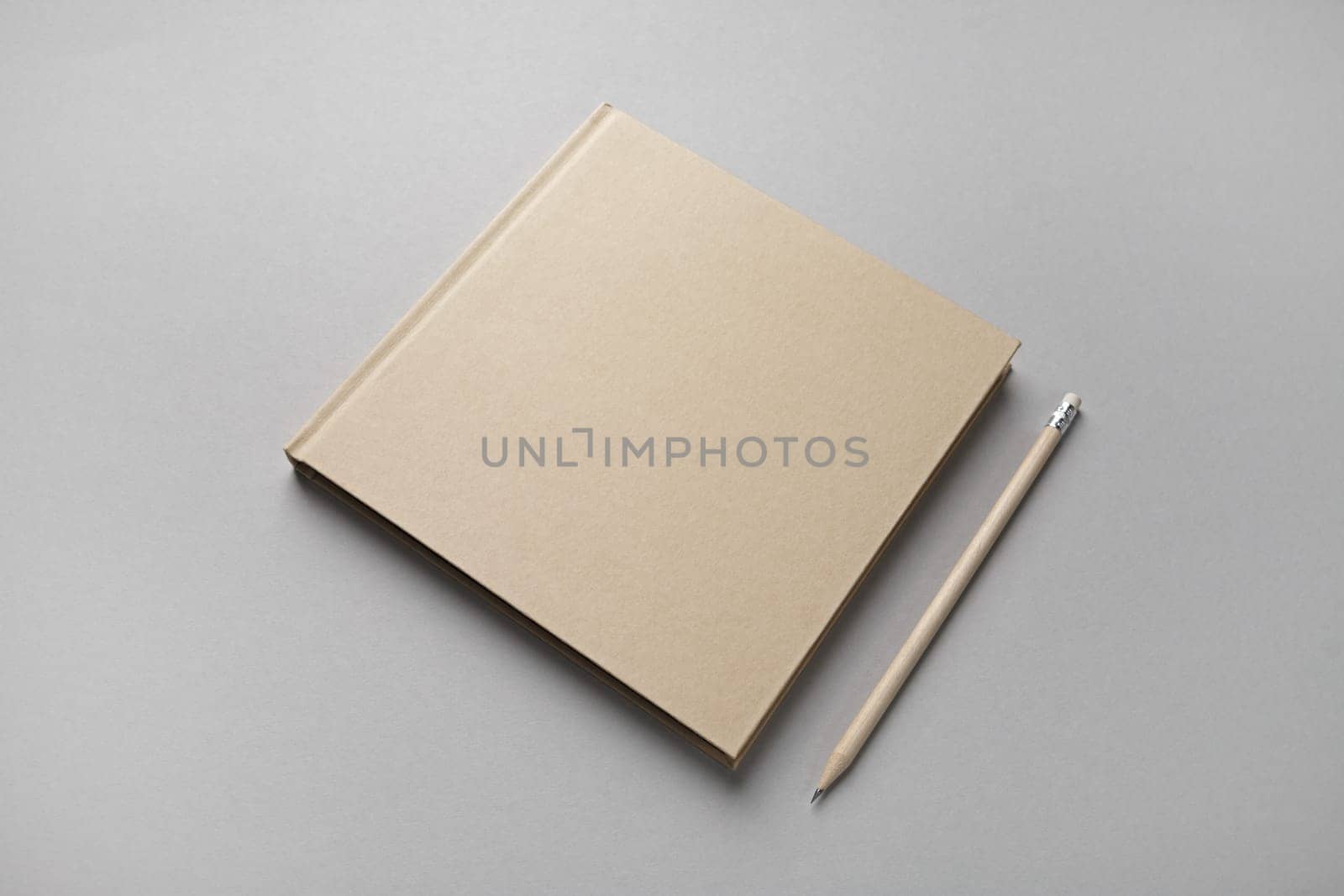 Photo of closed blank kraft brochure and pencil on gray paper background. Template for placing your design.