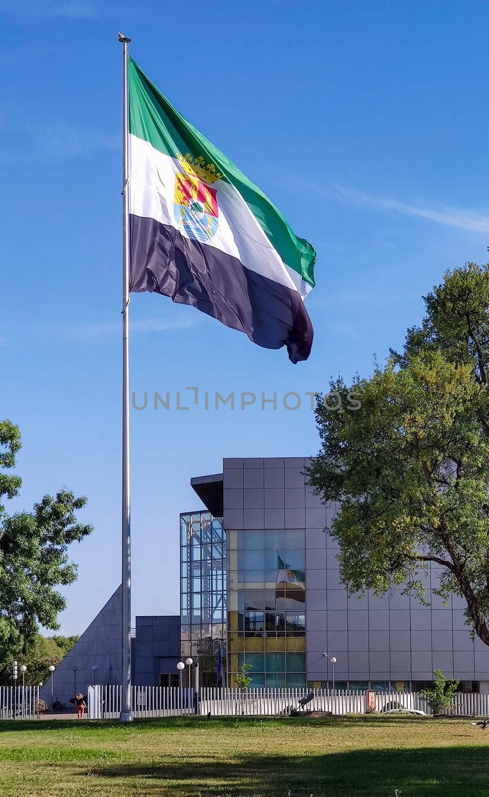 Merida, Spain - April 17th, 2023: Extremadura Region flag waving over blue sky. Lusitania Bridge roundabout, Merida, Spain