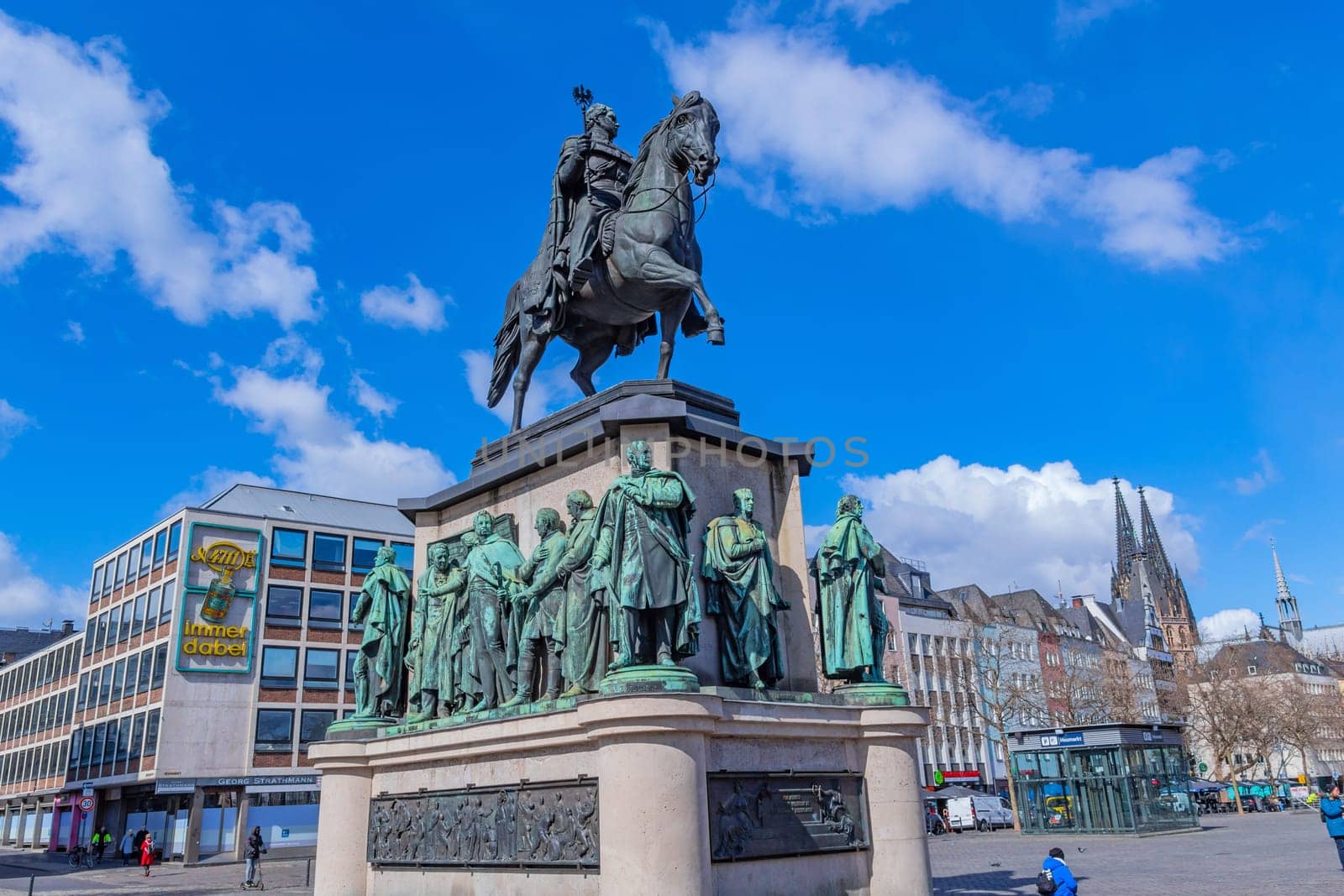 Cologne, Germany, March 27, 2023: Equestrian statue of Friedrich Wilhelm III monument on pedestal and people tourists walking down cobblestone square in historical city centre