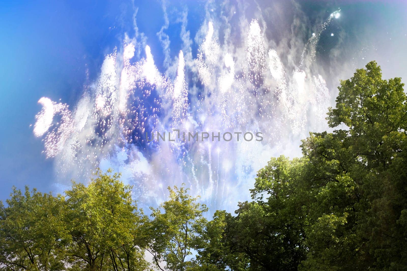Fireworks by day with white lights and sparkle particles in the foreground with tree group