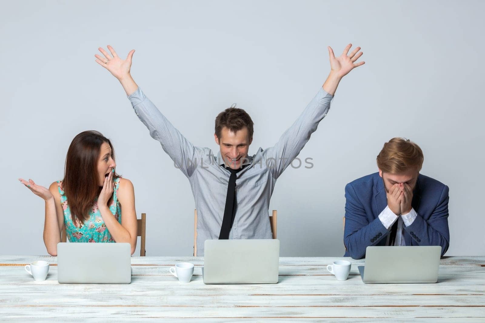 Business team working together at office on light gray background. all working on laptops. One man raising his arms enjoying good idea