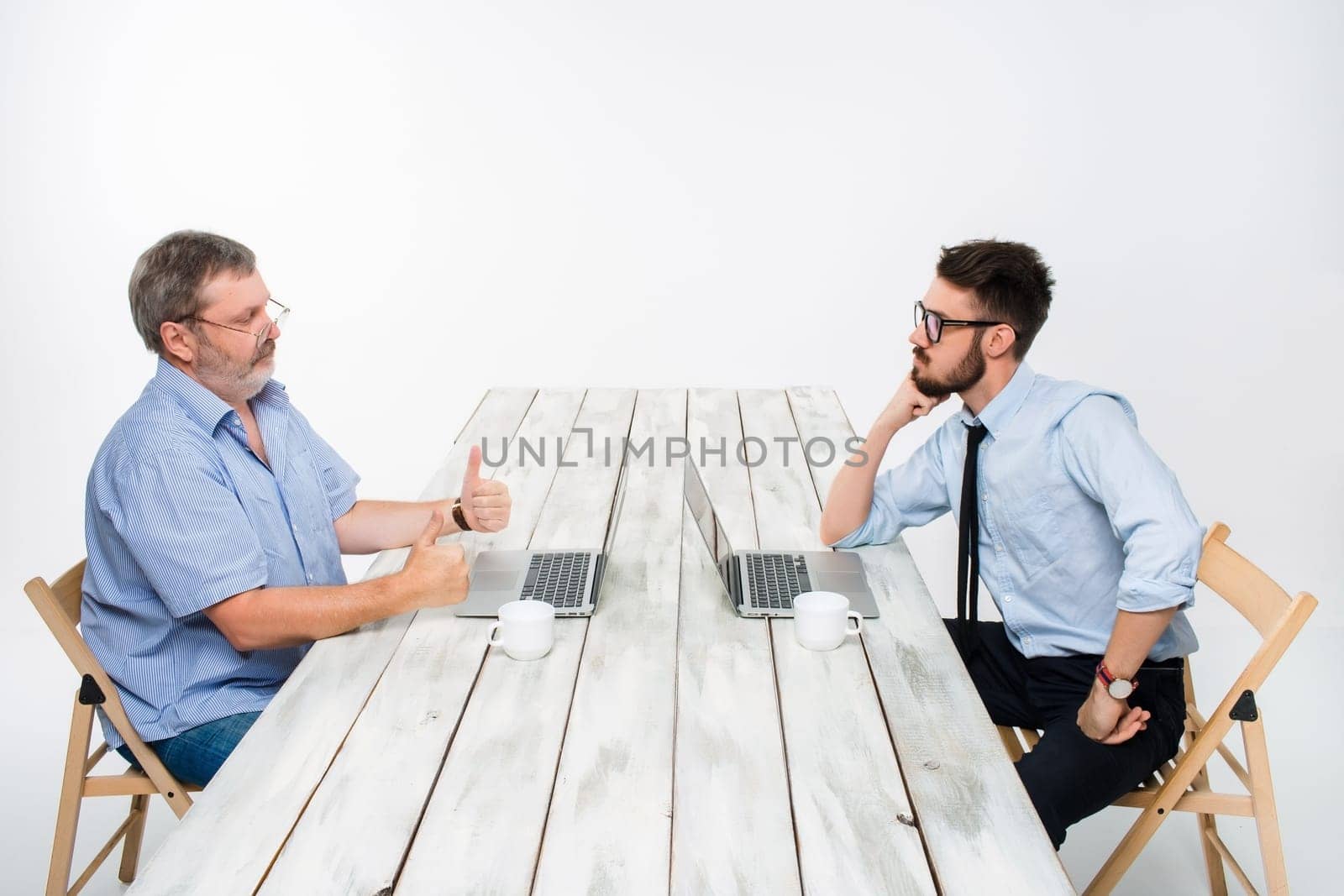 two colleagues working on project together on light gray background. They drinking coffee. happy man and jealous man. the concept of competition in the business