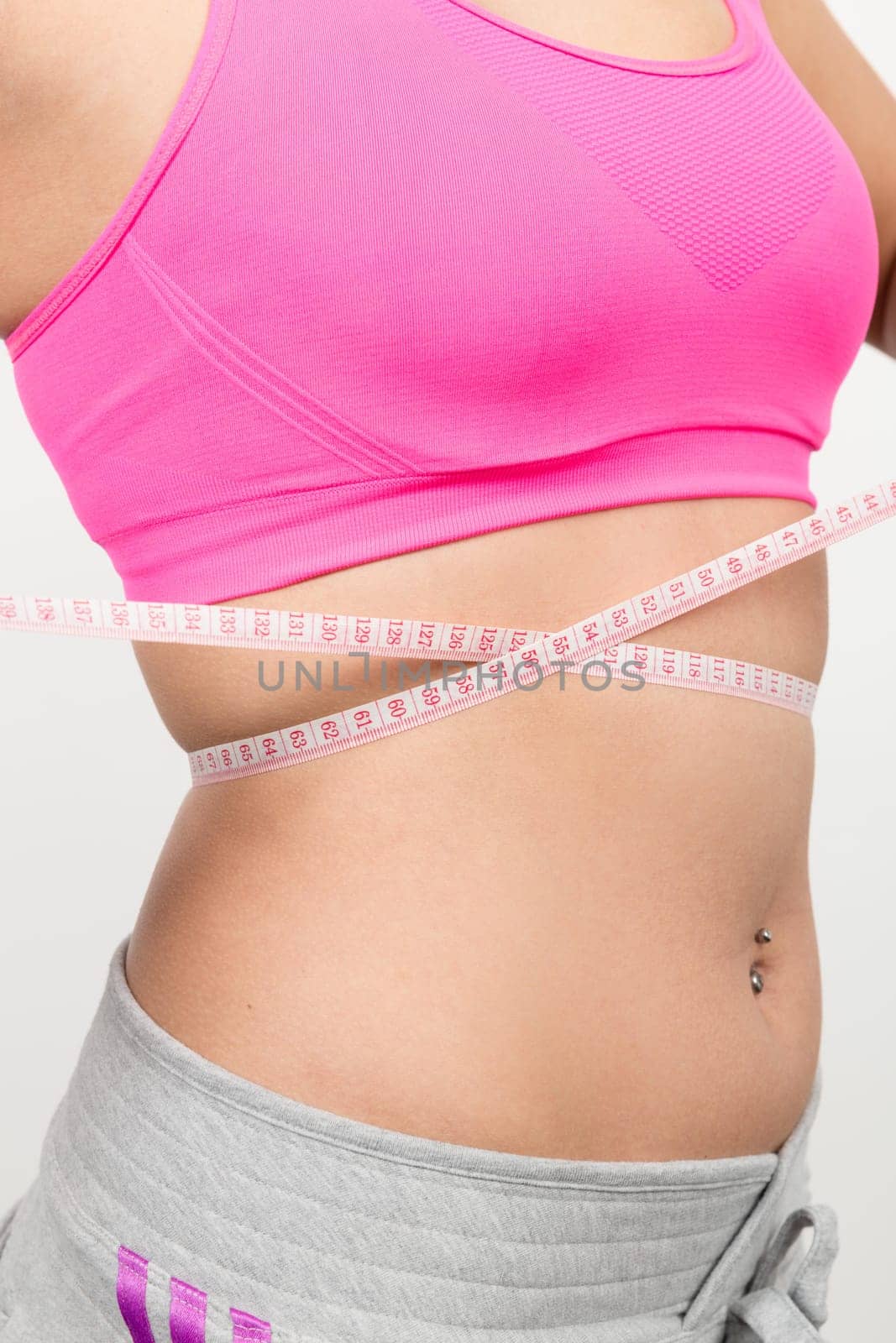 A young woman with a baunch navel piercing measures her waist with a band of measure