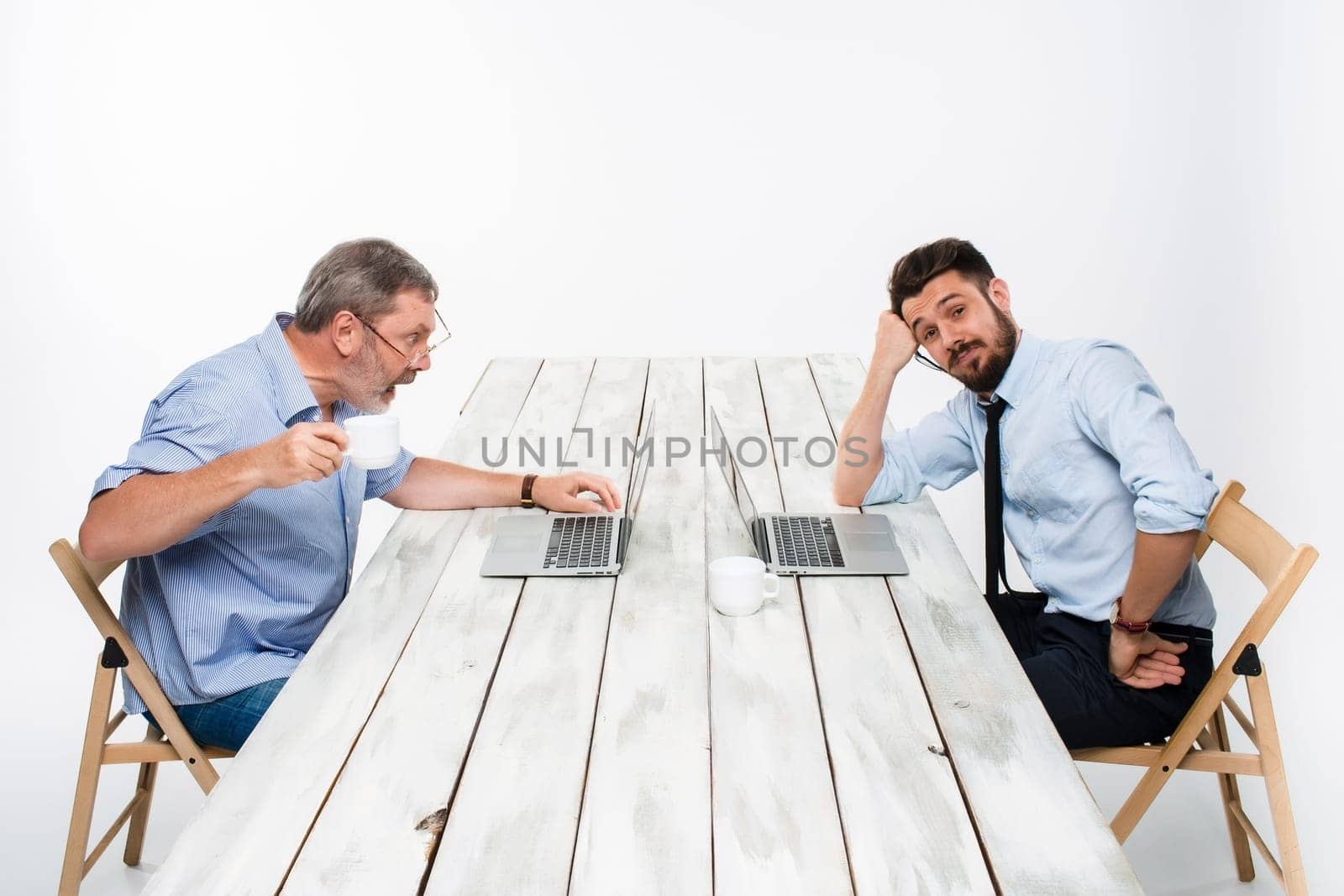 The two colleagues working together at office on light gray background. one  smiling man is satisfied, another man in stress looking at the computer screen.  the concept of competition in the business