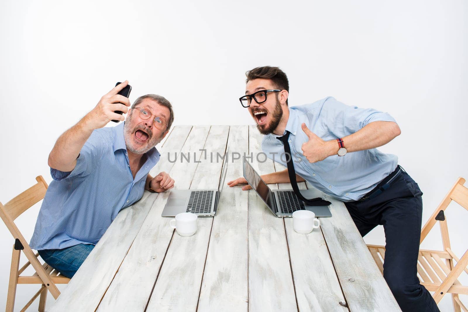 Two colleagues taking the picture to them self sitting in the office, surprised friends with glasses taking selfie with telephone camera  on white background