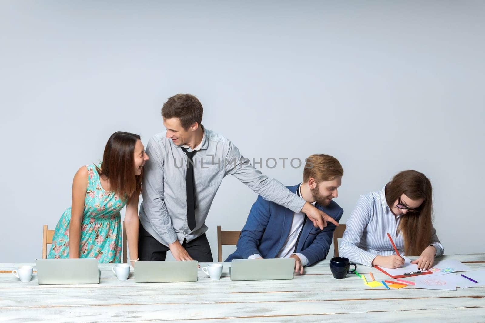 Business team working on their business project together at office on light gray background.  all smiling and looking at the boss. the boss is writing in a notebook. copyspace image.
