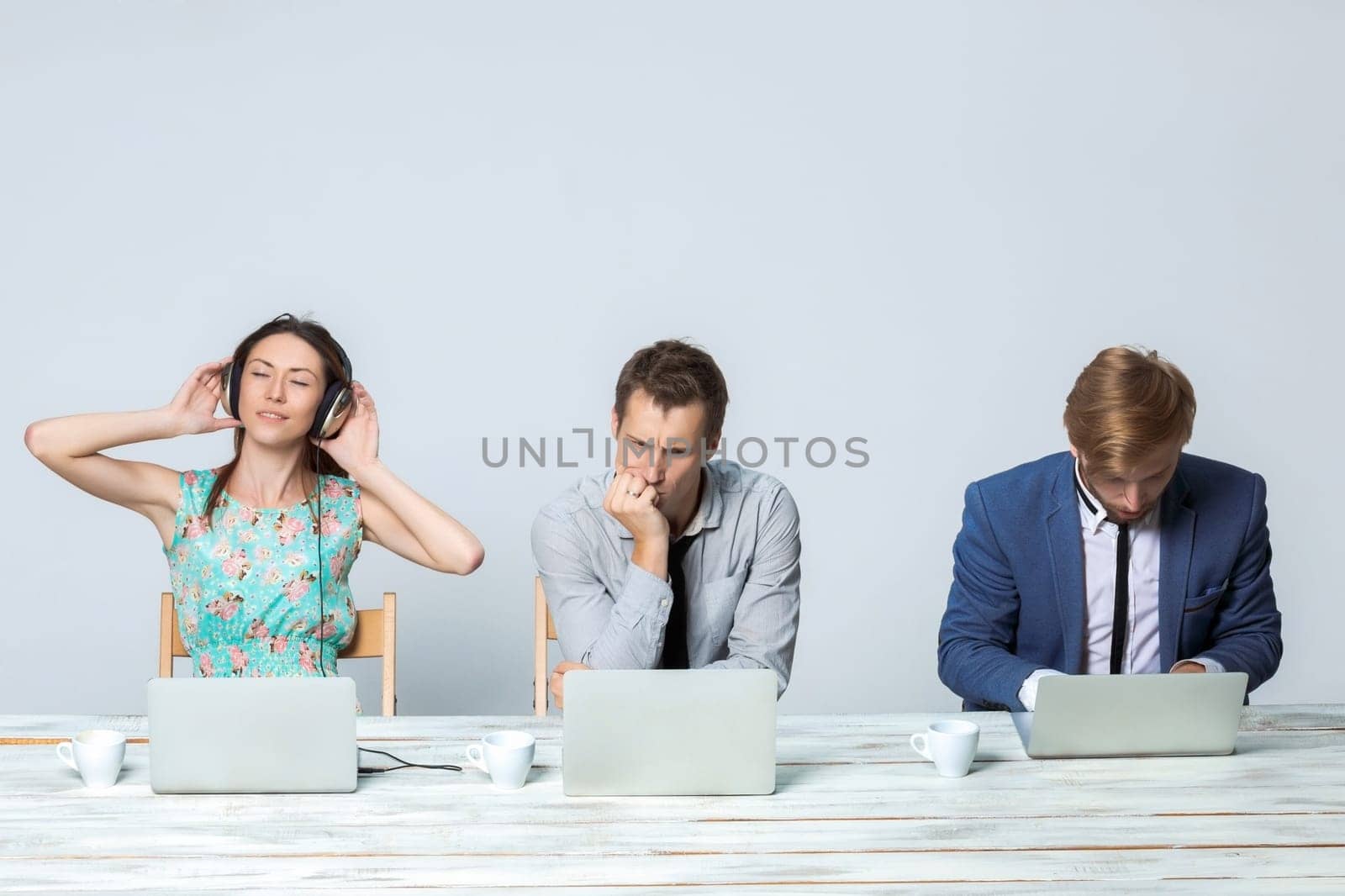 Business team working together at office on light gray background. all working on laptops. girl in headphones enjoying the music