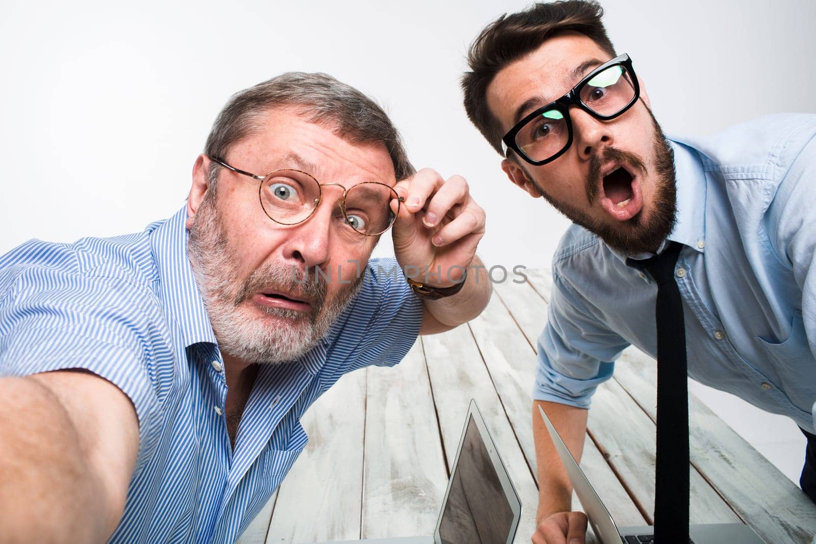 Two colleagues taking the picture to them self sitting in the office, surprised friends with glasses taking selfie with telephone camera  on white background