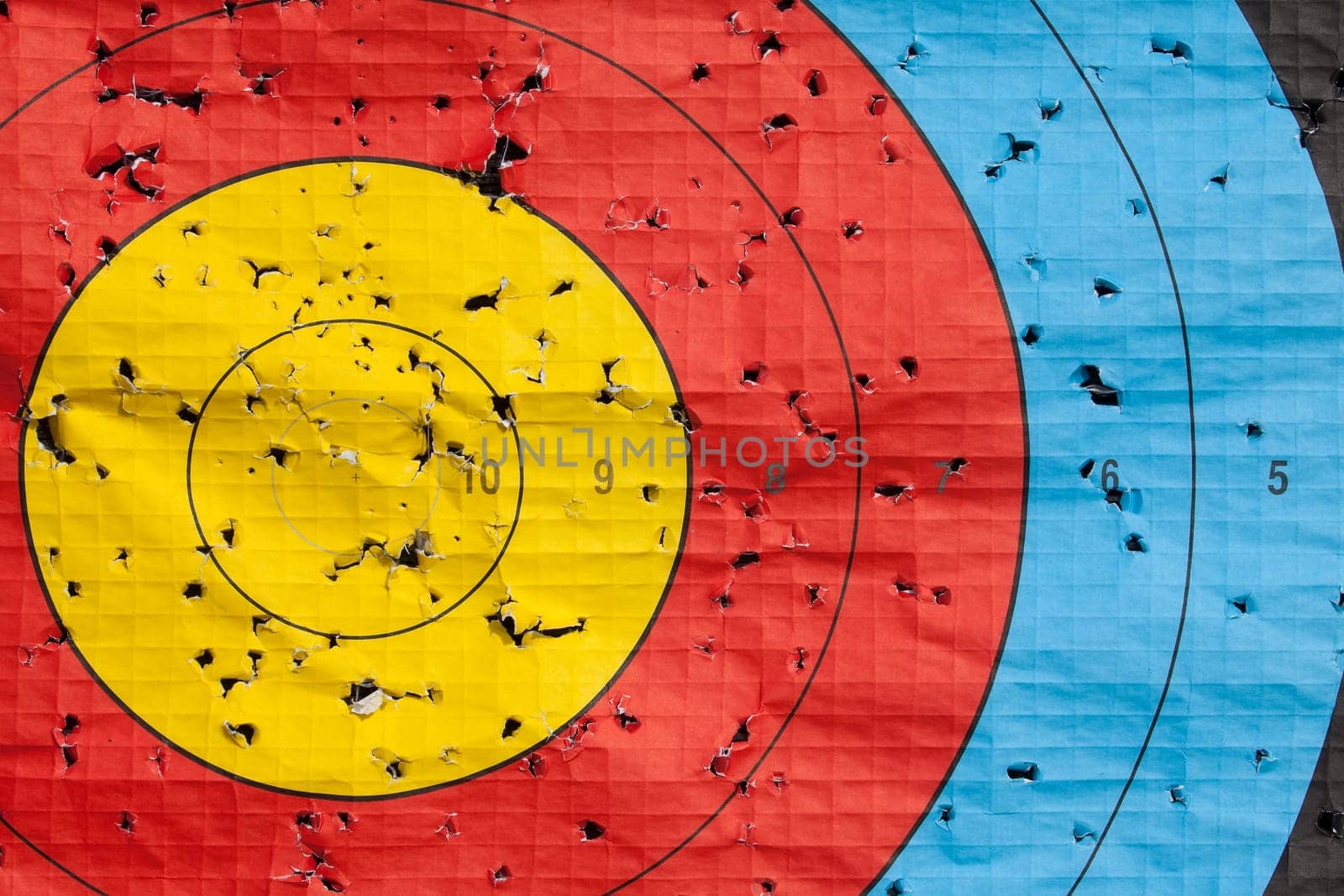 Archery target close up with many arrow holes in gold red blue and black