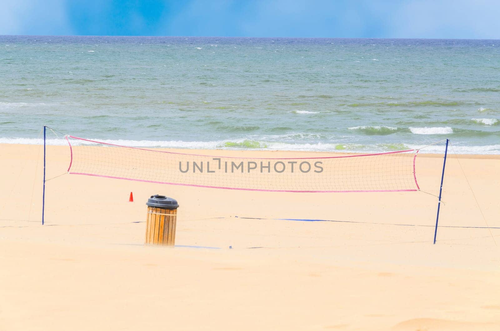 Empty beach in the foreground a volleyball net the blue sea and sky.