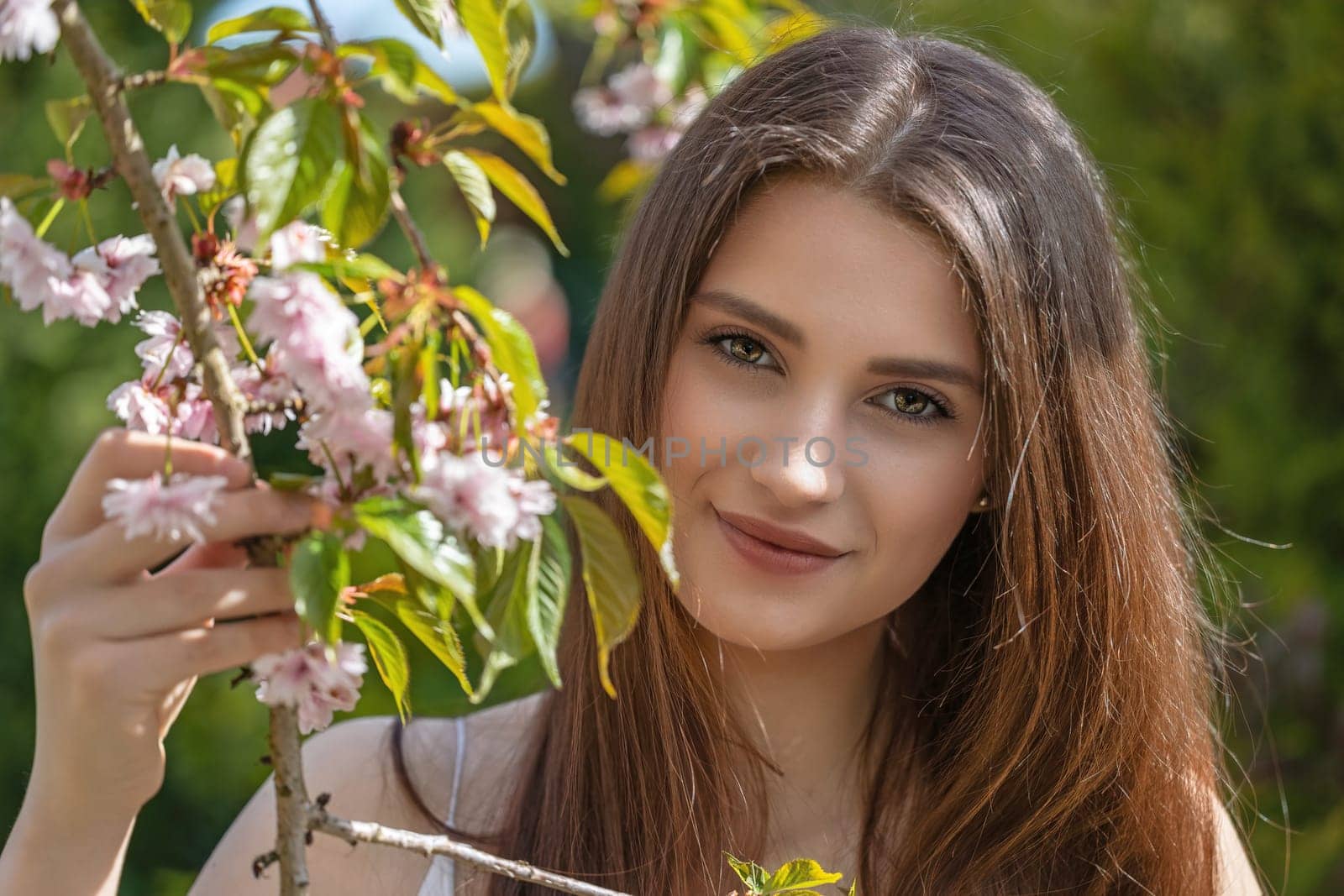 Attractive brunette girl posing on camera holding a sprig of cherry blossoms. Horizontally.