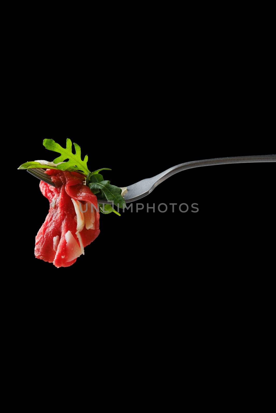 Slice of marbled beef carpaccio on fork over black background