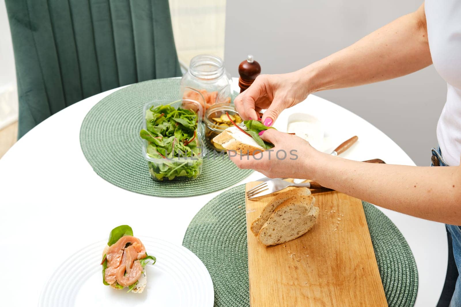 Hands of unrecognizable woman puts fresh salad on sandwich