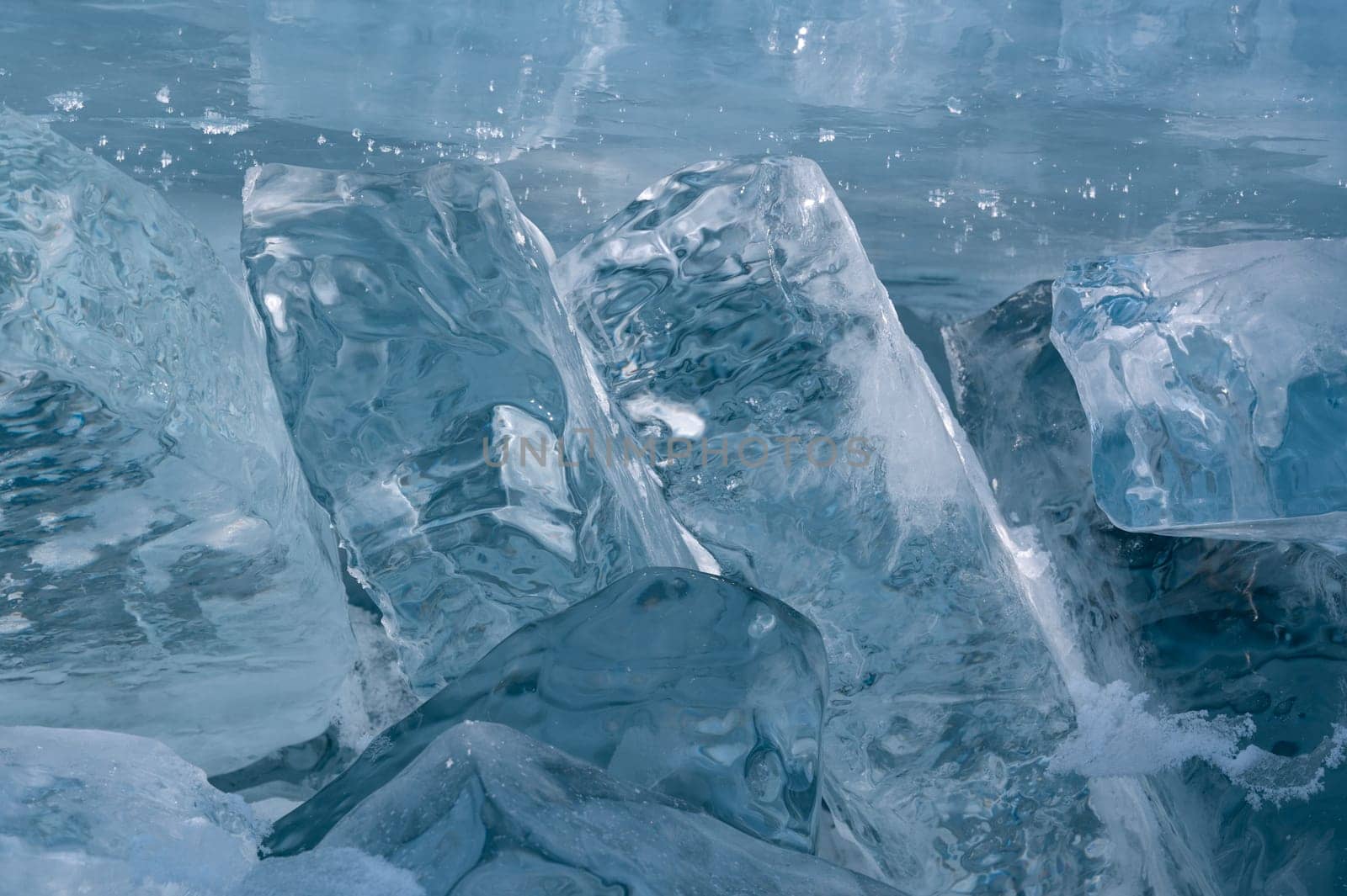 Transparent blue ice floes piled in ice hummocks against a blue sky on a sunny day. Unusual winter landscape of the frozen lake Baikal. Natural cold background. Siberia, Russia.