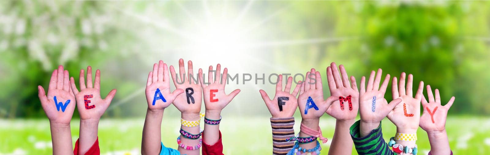 Children Hands Building Colorful English Word We Are Family. Sunny Green Grass Meadow As Background.